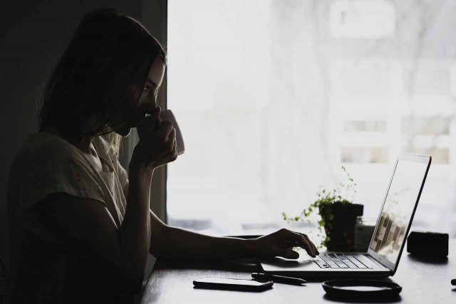 Une femme buvant un café devant l'écran d'un ordinateur