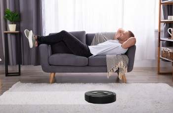 Jeune homme allongé sur un canapé avec un aspirateur robotique sur un tapis