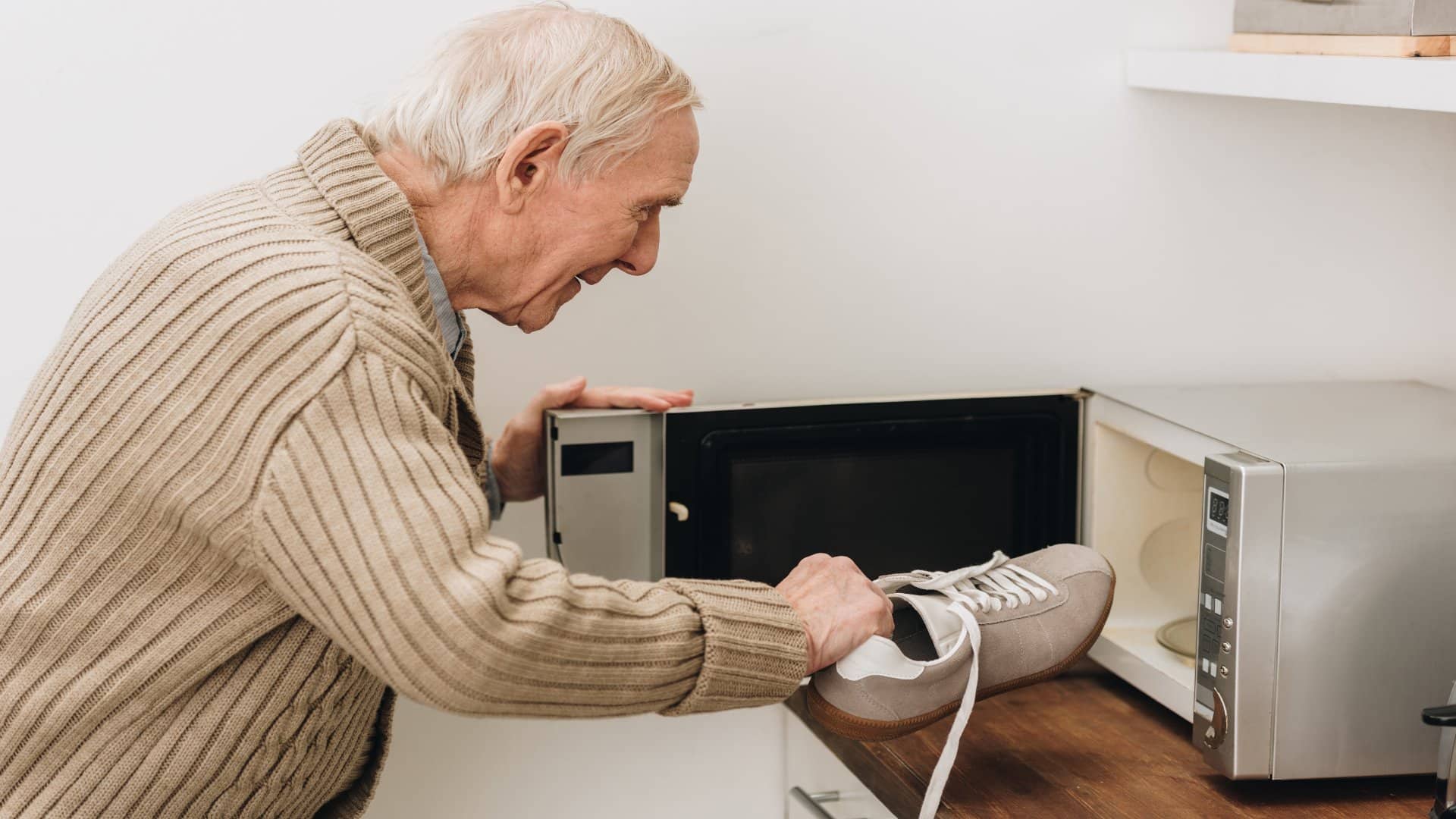 A senile old man places a shoe in a microwave.