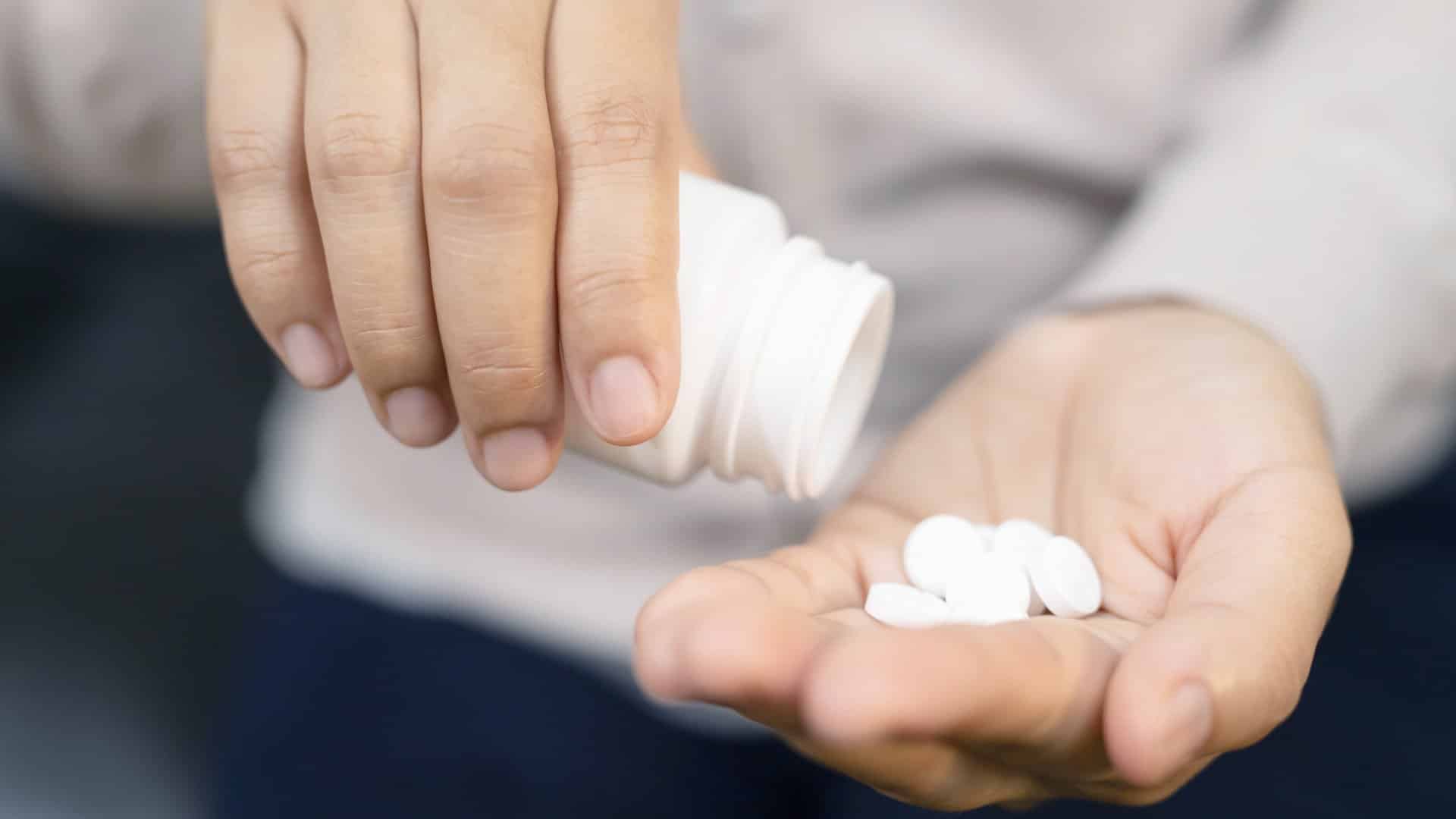 A woman pours many pills into her left hand.
