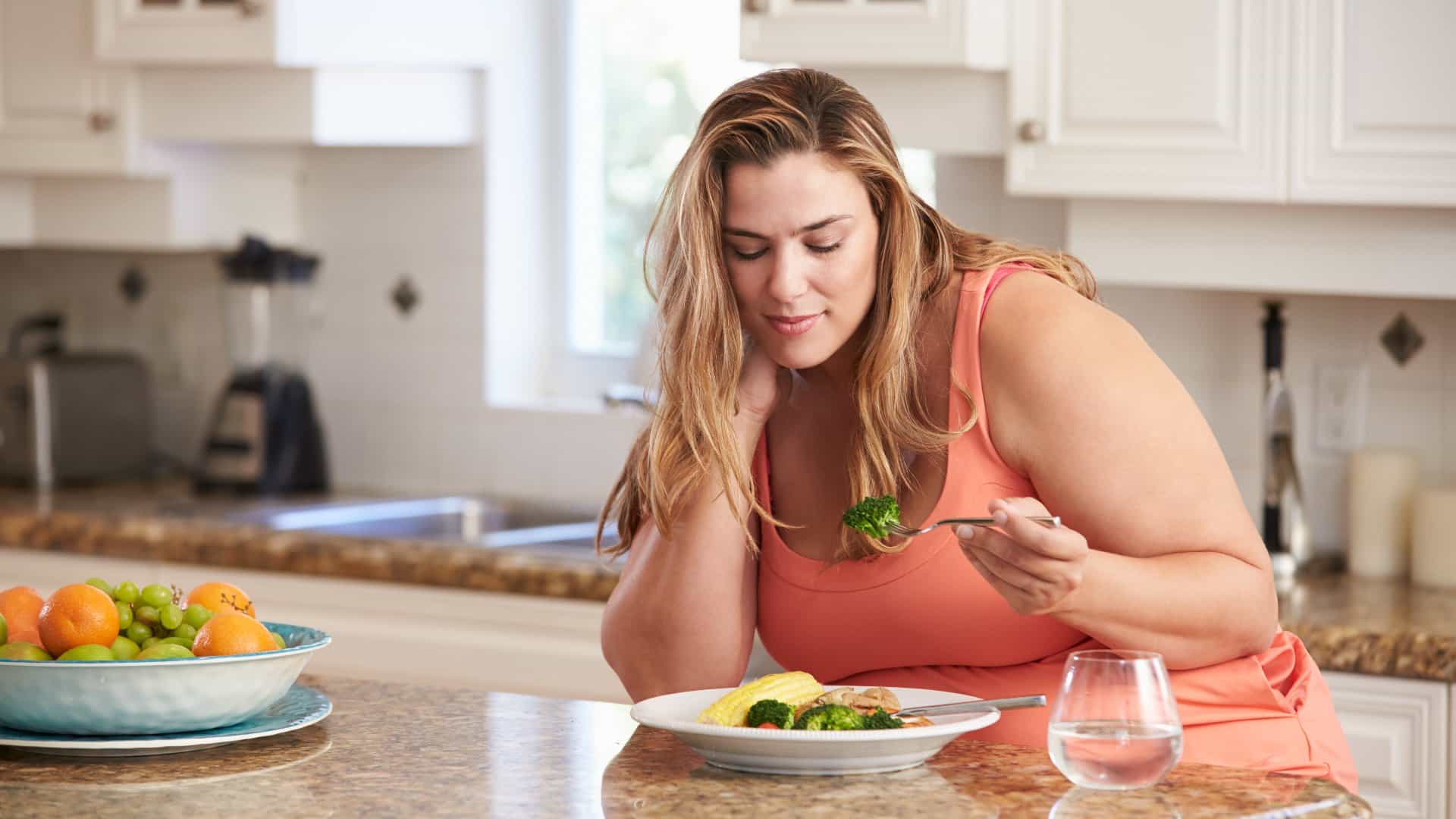 Femme en surpoids mangeant un repas dans la cuisine