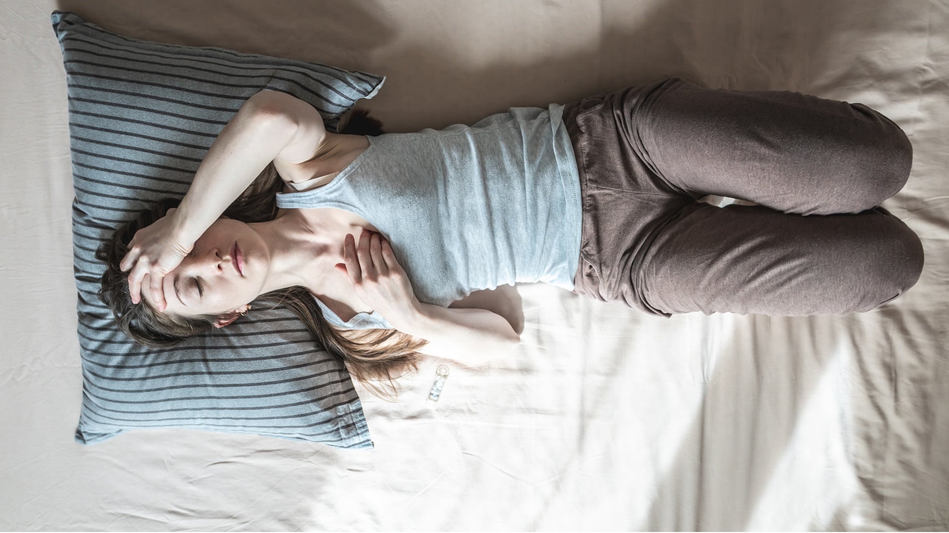Une femme allongée dans son lit tient sa tête avec sa main à cause d’un mal de tête intense.
