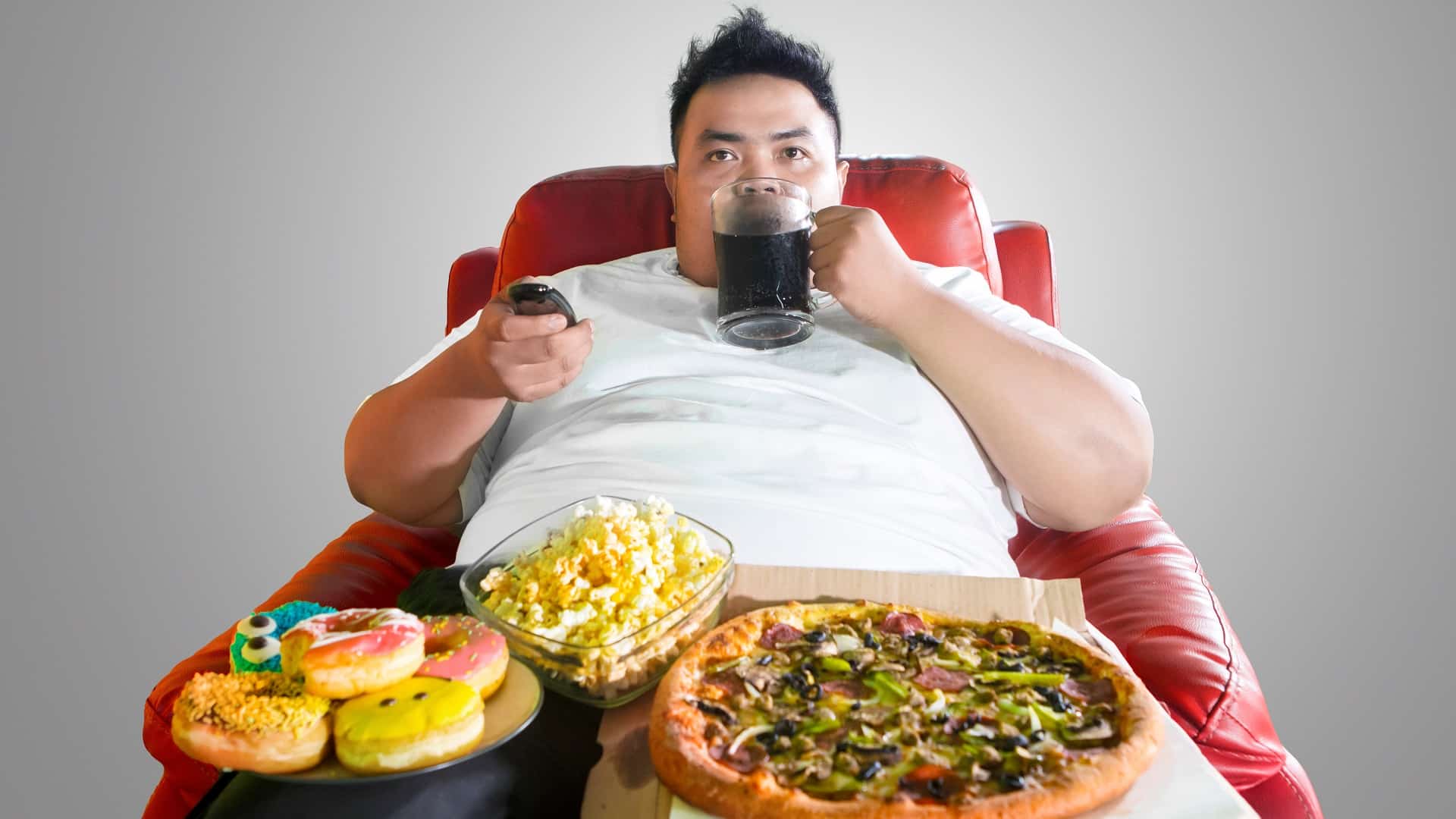 Un jeune homme obèse regarde la télévision tout en mangeant.