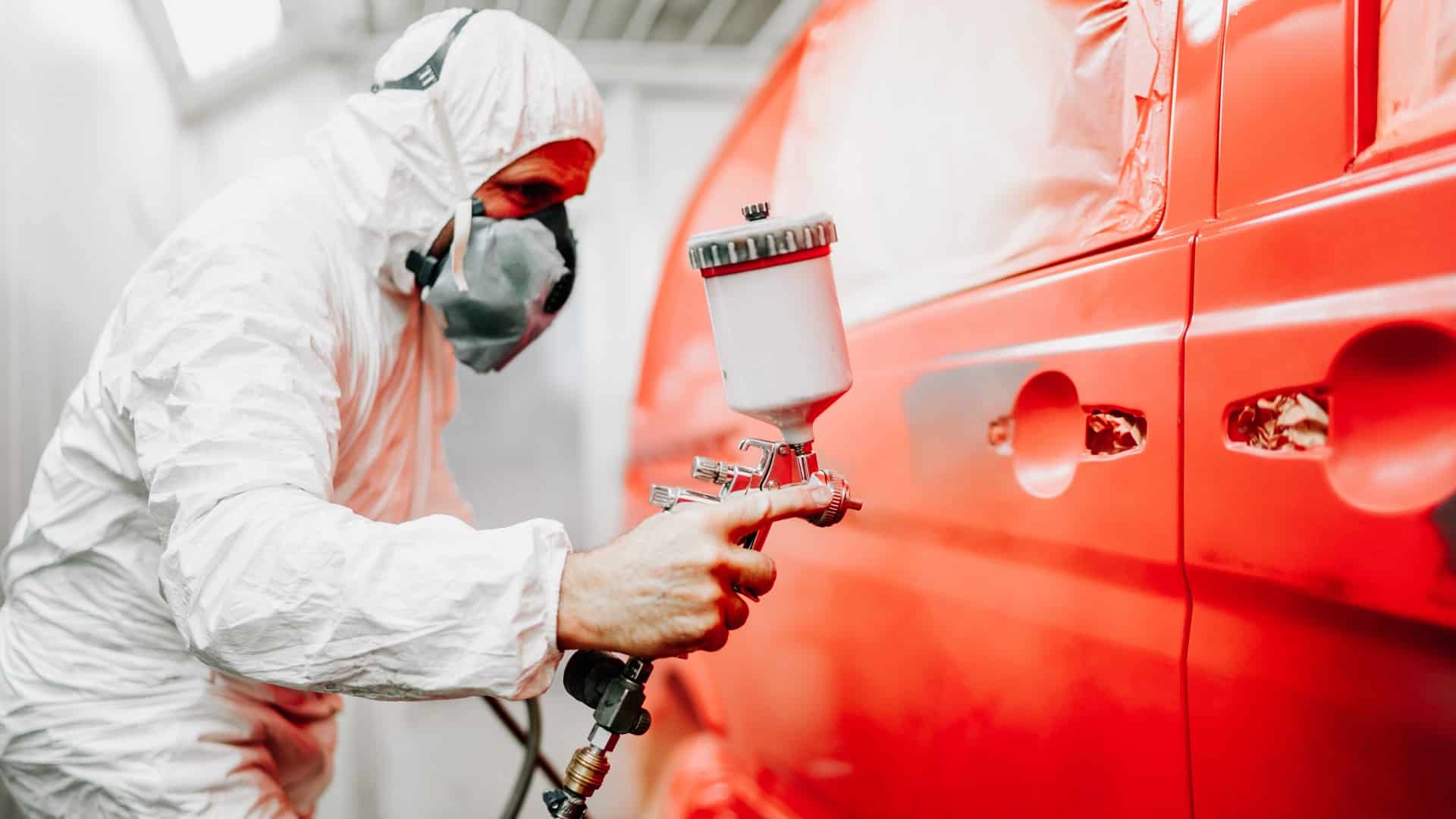 Un mécanicien qui peint la carrosserie d'une voiture rouge.